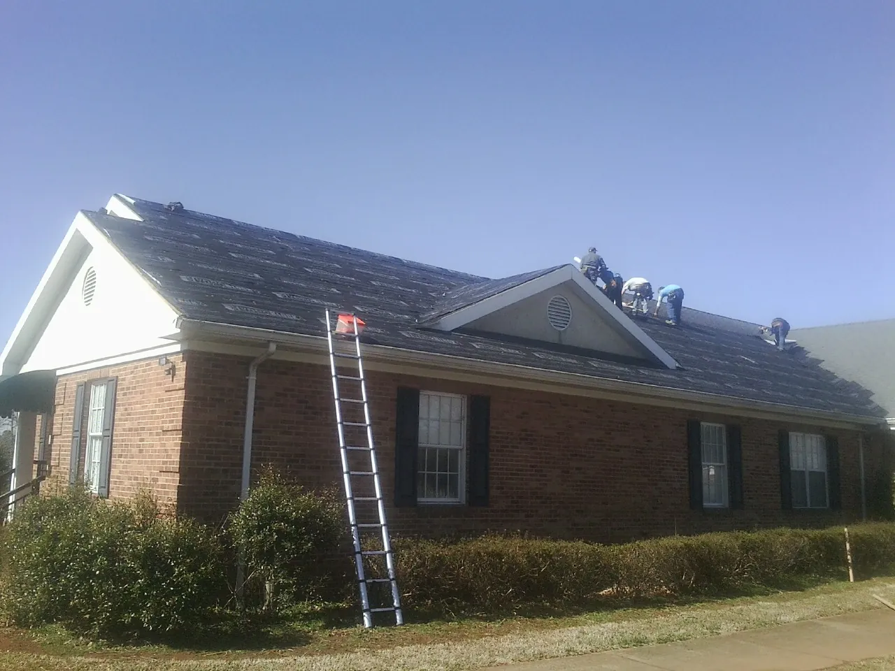 Crew tearing shingles off a brick ranch roof with a ladder set — Emergency Roof Repair work by our crew in Clarington