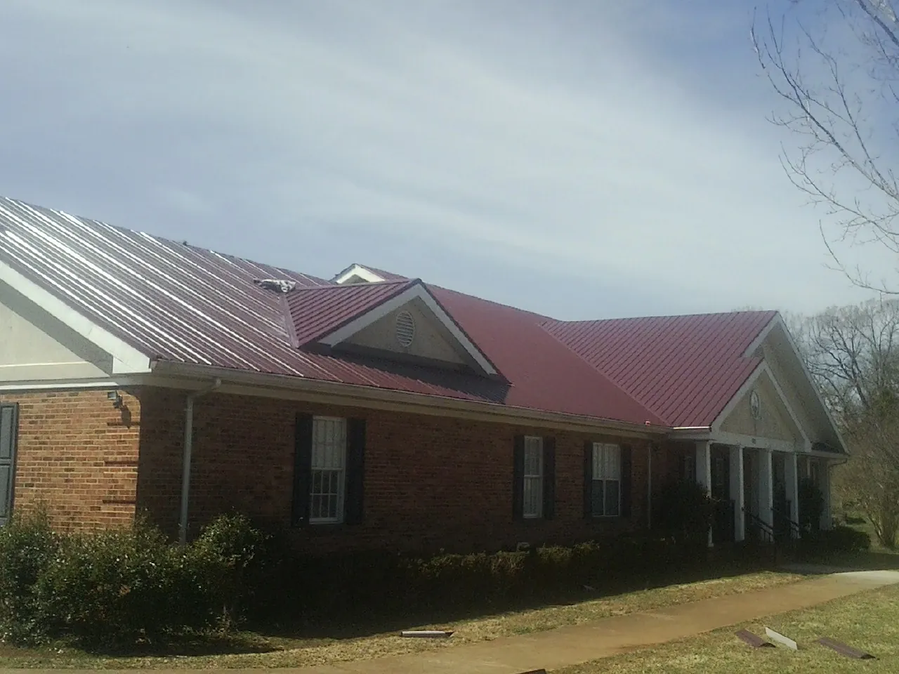 Red metal roof with gabled entries on a long brick building, from a Hail Damage Roof Repair job in Clarington