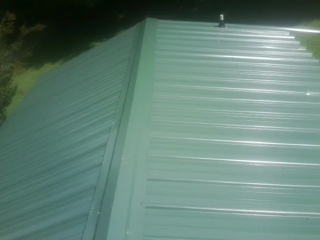 New green metal panels meeting at the ridge of a roof — Flat Roof Repair work by our crew in Clarington