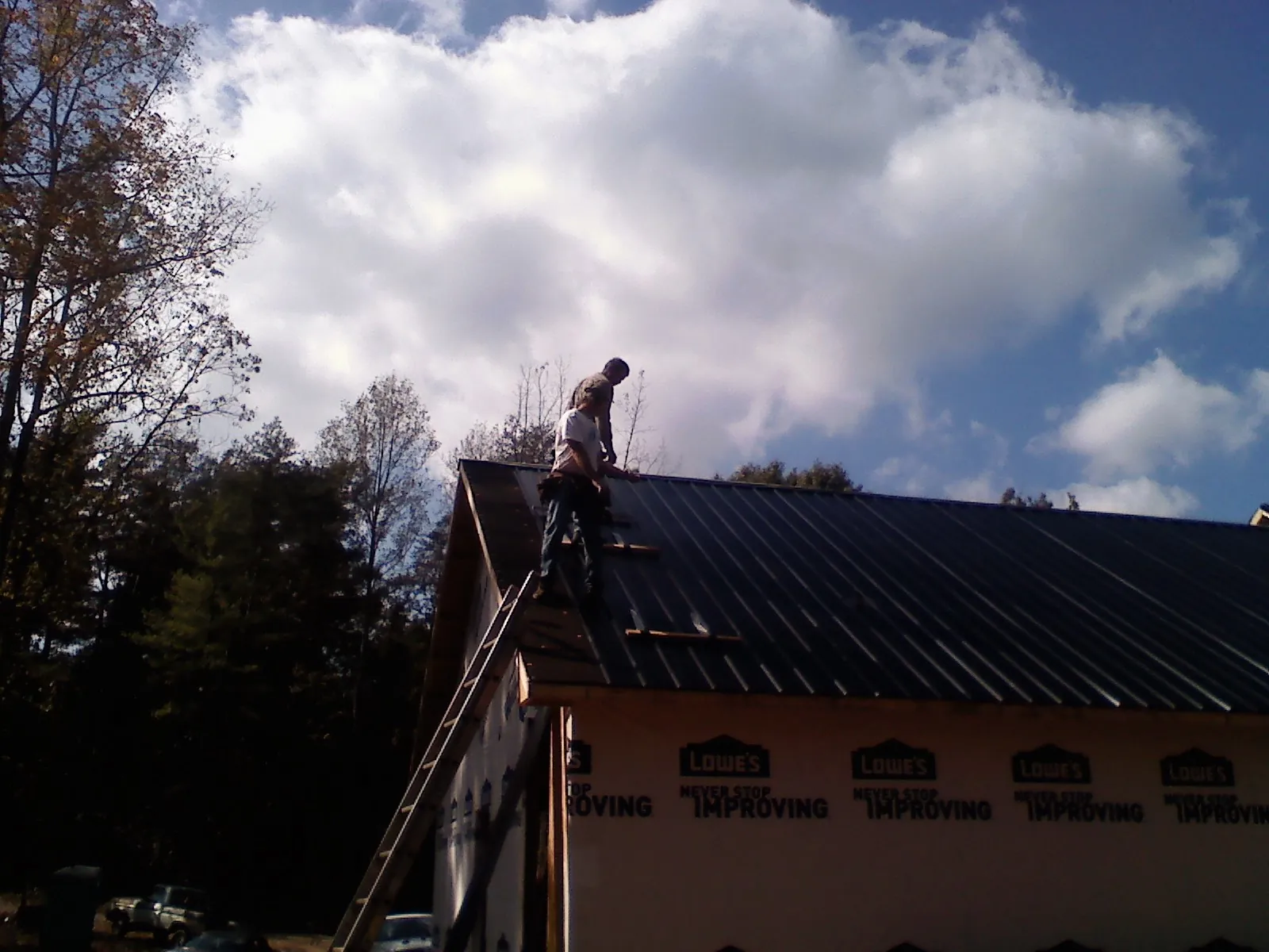 Roofer fastening dark metal panels high against a cloudy sky, from a Roof Inspection job in Clarington