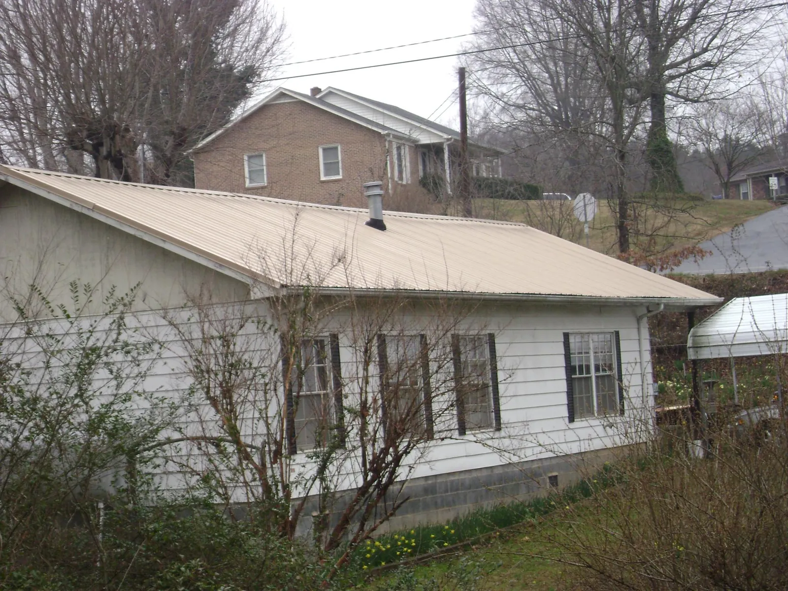 Tan metal roof on a white sided house set into a hillside — Commercial Roofing by Roofing Brothers in Clarington
