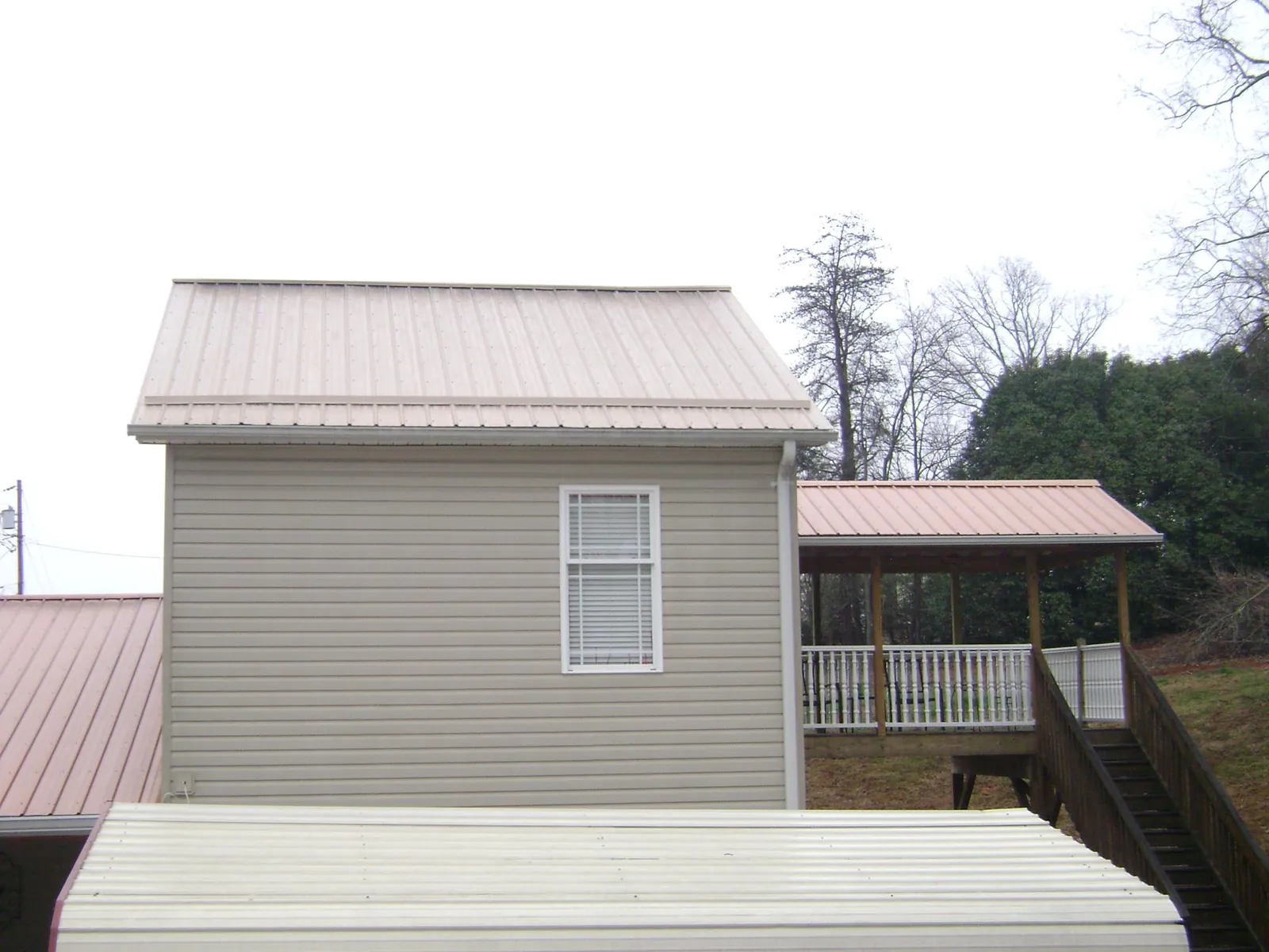 Tan metal roofs on a two story addition and attached porch, from a Roof Replacement job in Clarington